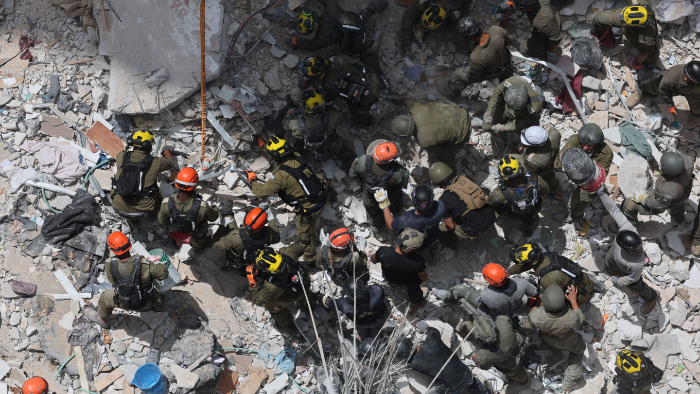 Members of Israel's Home Front Command search for missing people under the rubble of a partially collapsed residential building