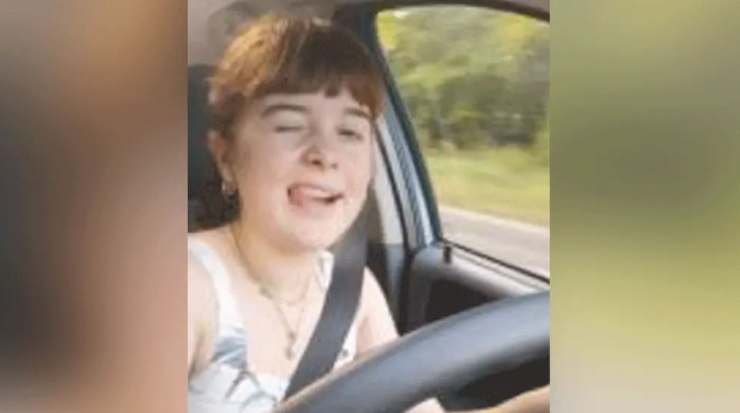 A selfie image of a young woman winking at the camera with her tongue out while driving 