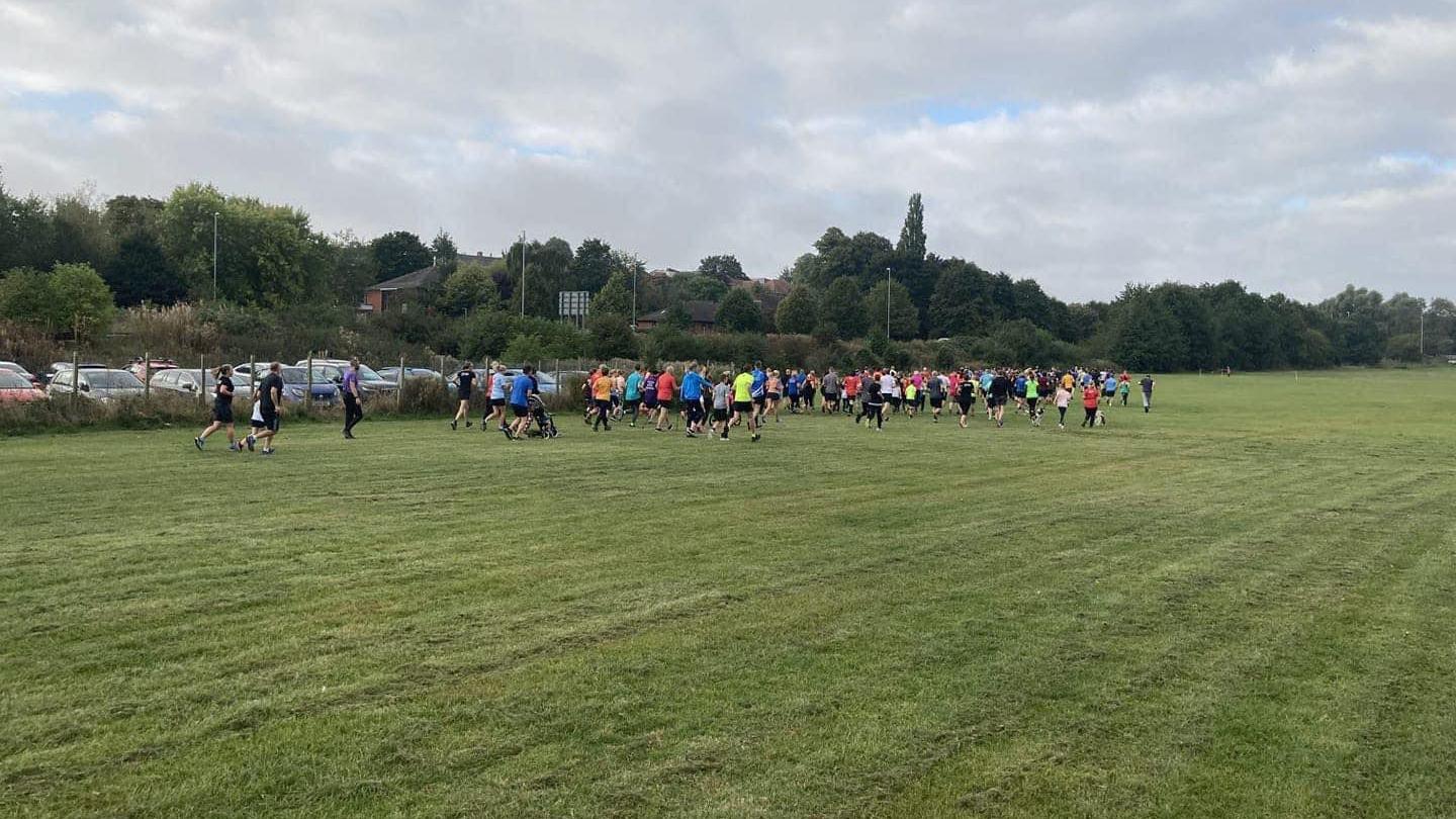 Lots of runners in different coloured clothes jogging through the park 