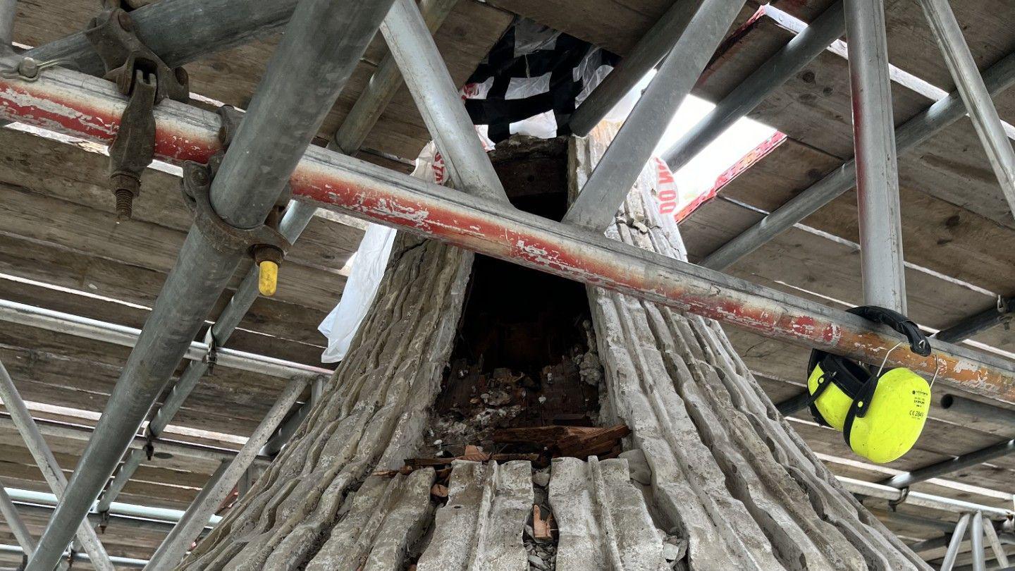 The exposed roof of Brighton's Royal Pavilion. Brown shards of timber are inside a long, rectangular hole in the roof. The roof is covered by scaffolding.