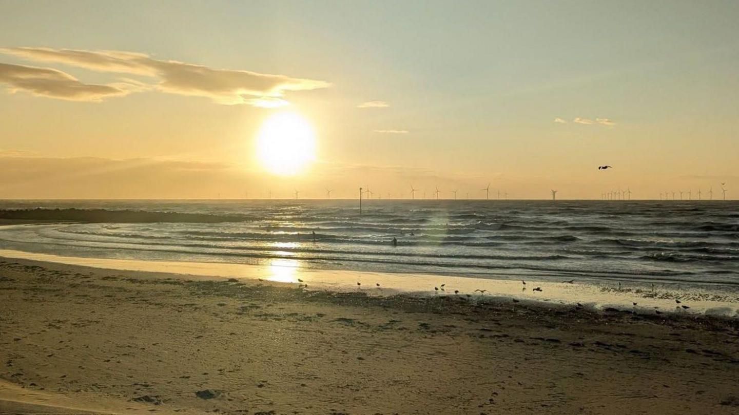People in the sea as the sun sets over Leasowe Bay, Wirral