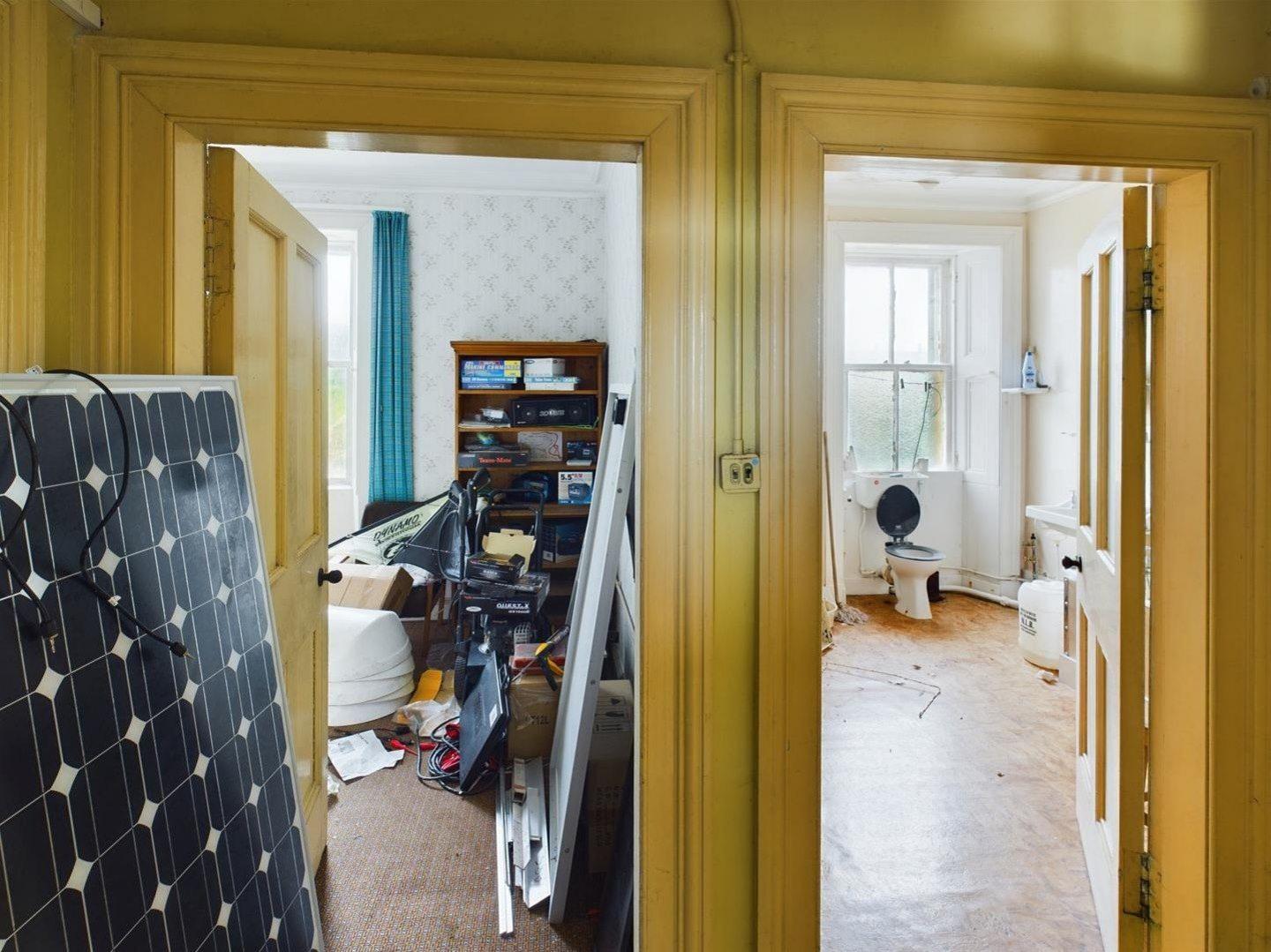 Interior showing two doorways leading to a bedroom and a bathroom with a solar panel resting against a wall in the hallway