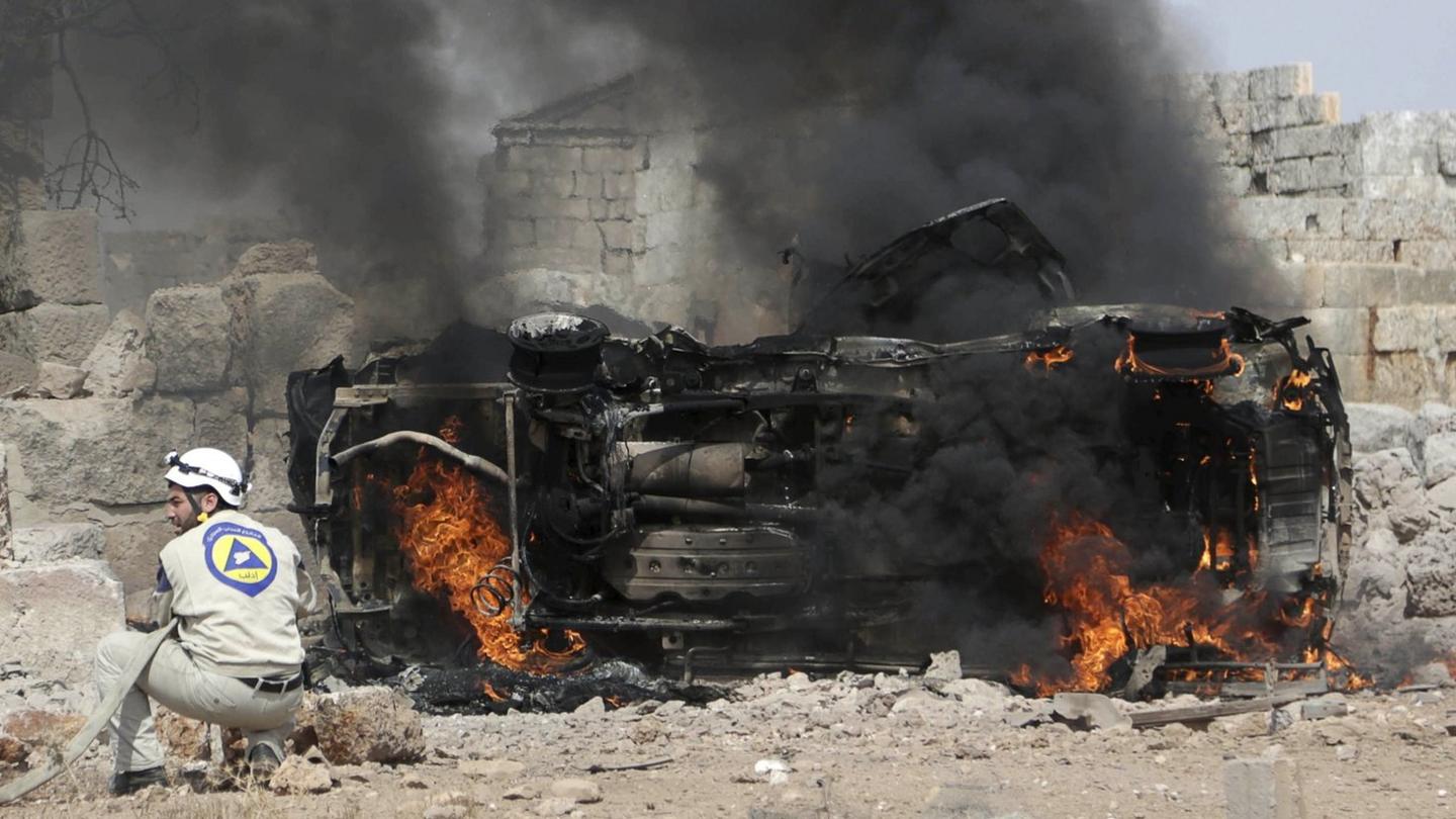 A man crouches beside a vehicle that rebel fighters say was targeted in a Russian air strike in Hass, in Idlib province, Syria (1 October 2015)