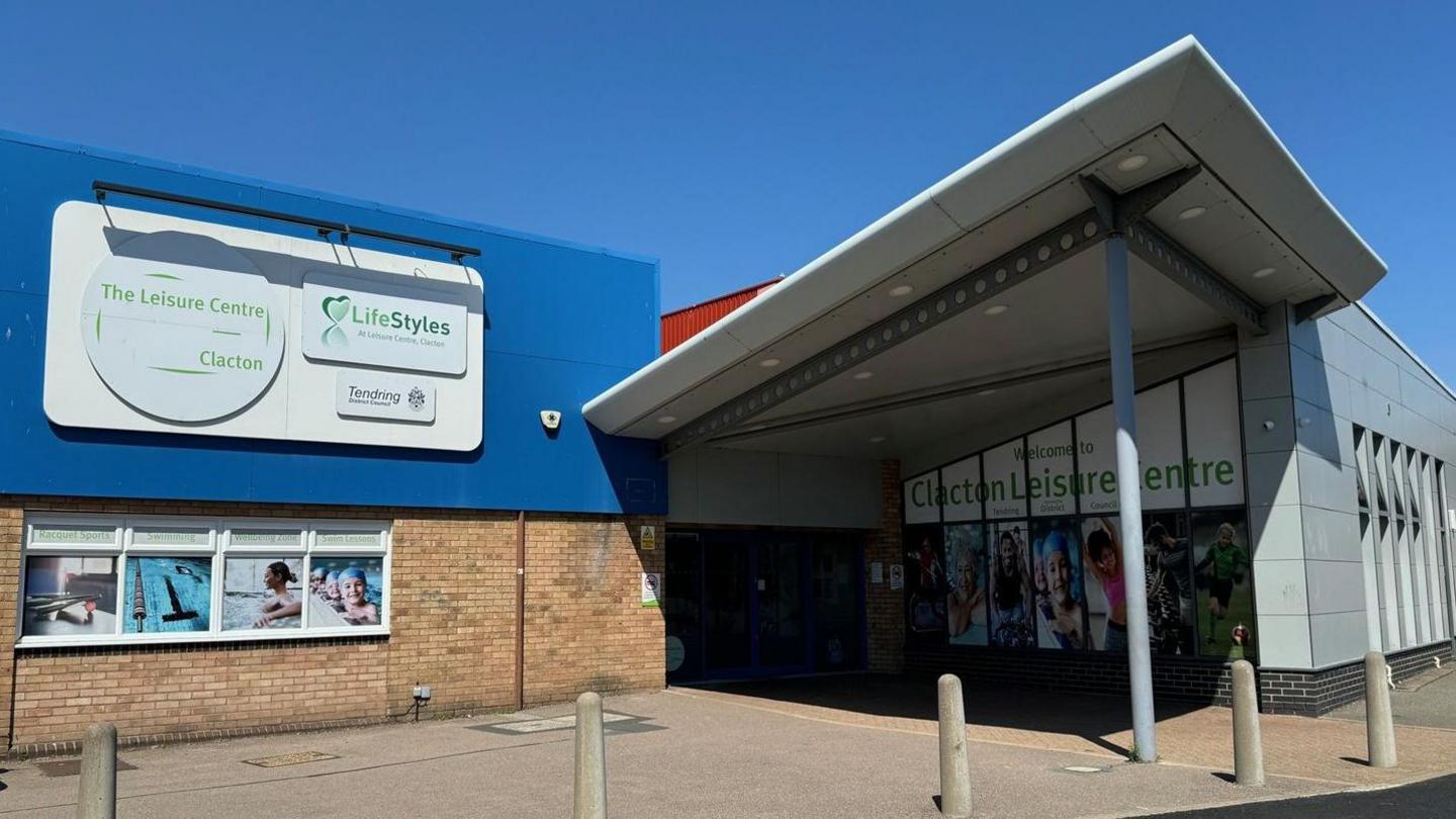 The entrance to Clacton Leisure Centre, which is a grey building that has a large canopy above the doors, held up by a column.