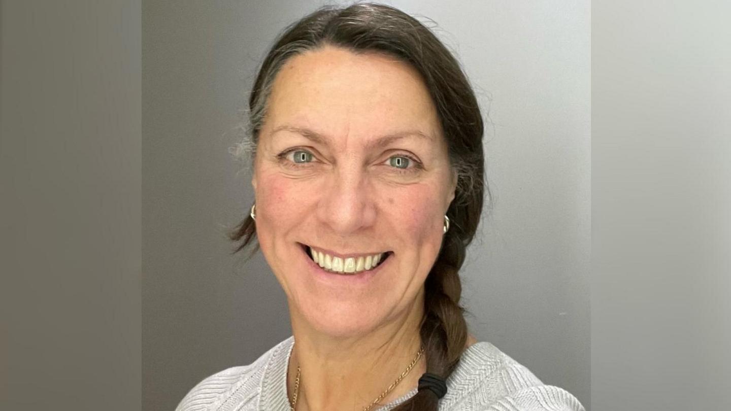 Dr Suzanne Smith smiling in front of grey background. She has brown hair and blue eyes.