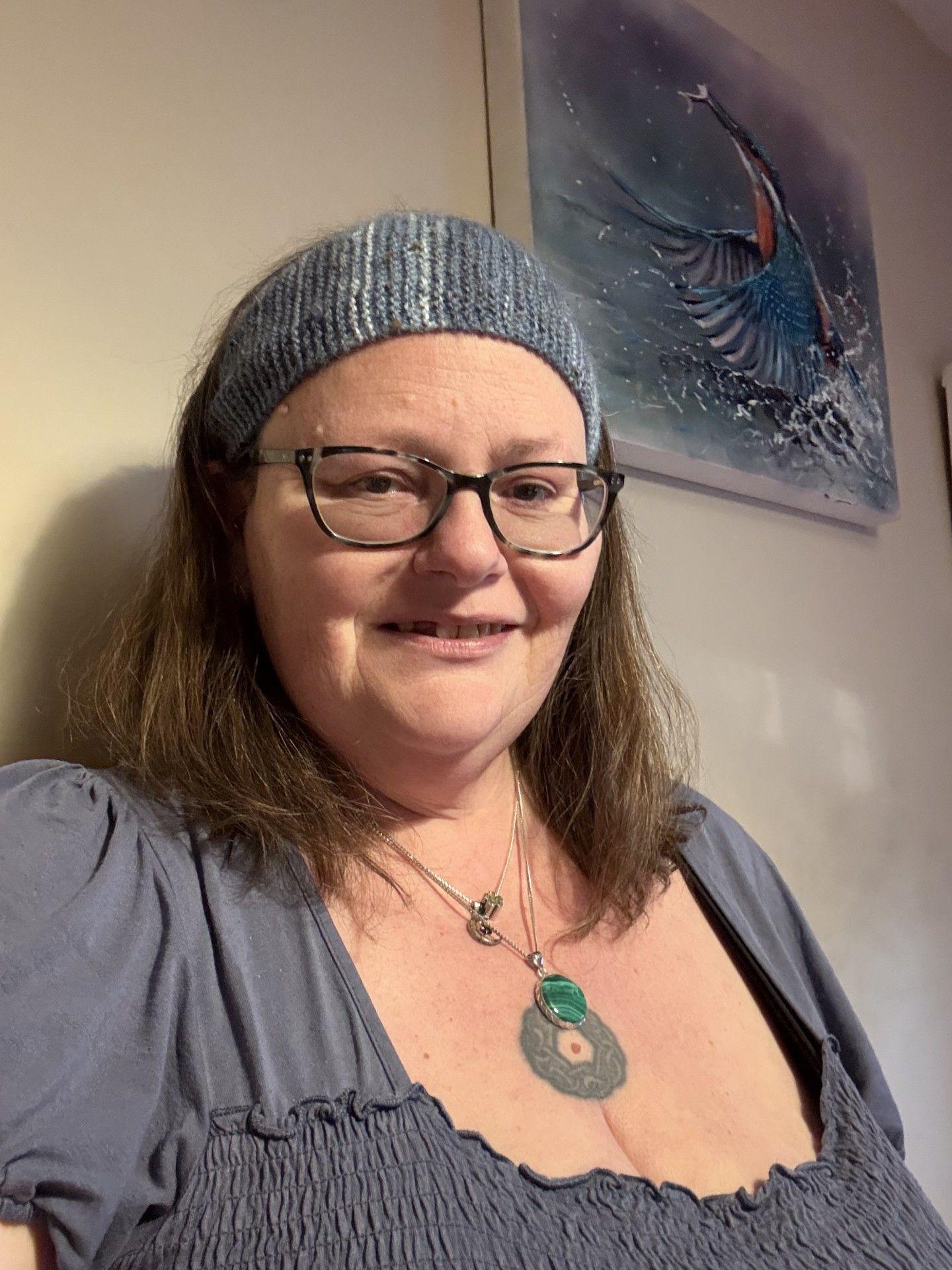 Selfie of Sarah Bodger smiling, wearing a blue headband, glasses, a necklace and a blue top.