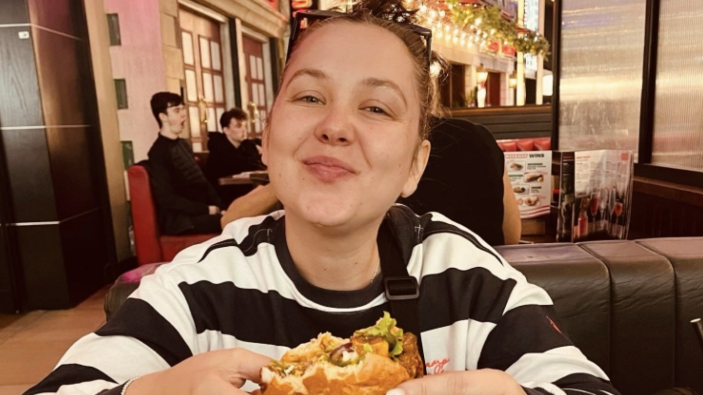 Woman in restaurant in black and white striped jumper eating hamburger