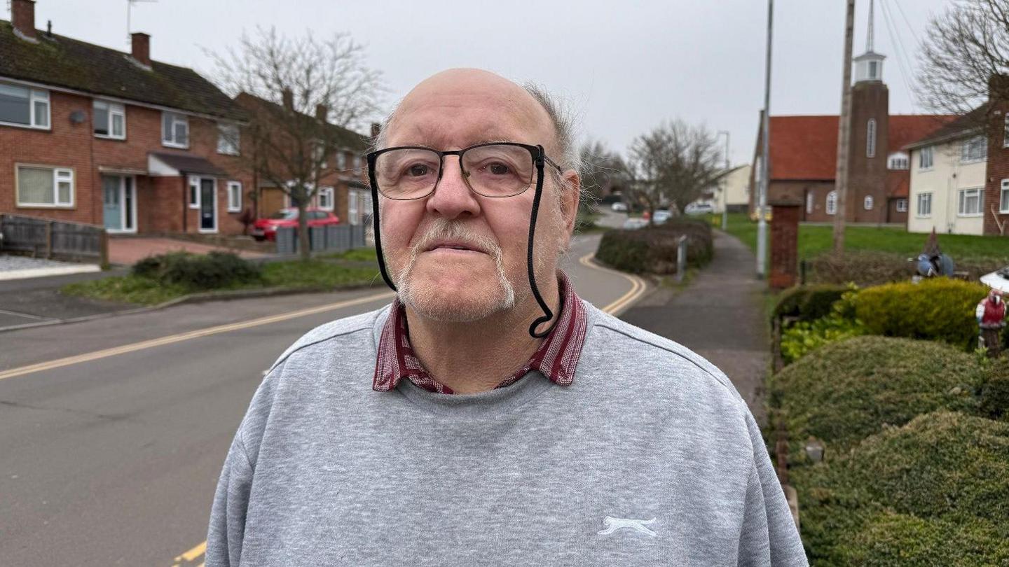 Derek Moore wearing a grey jumper looks at the camera with Eastwick Road in the background