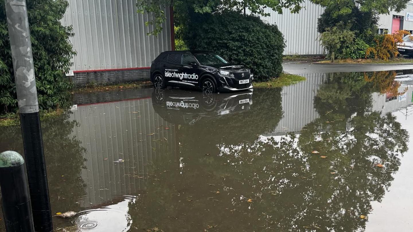 A black Isle of Wight Radio car in a car park surrounded by flood water.