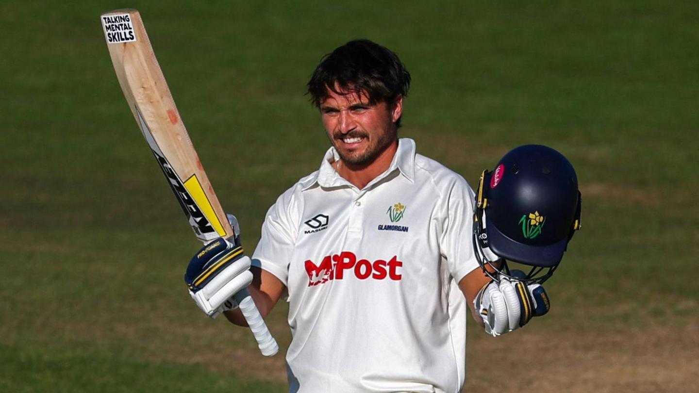 A smiling Kiran Carlson acknowledges the crowd with bat in one hand and helmet in the other