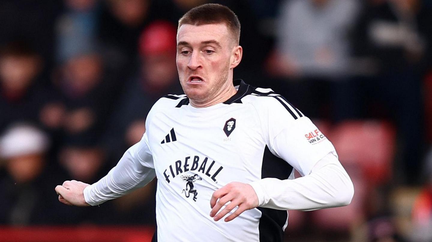 Ryan Watson on the ball for Salford City with his arms out.