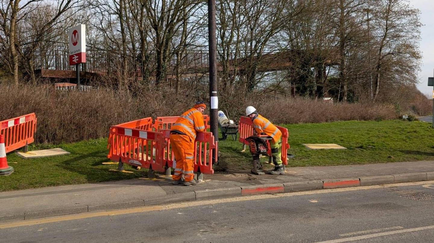 Workmen dressed in orange and yellow hi-vis put up a telegraph pole on a road in Garforth, Leeds