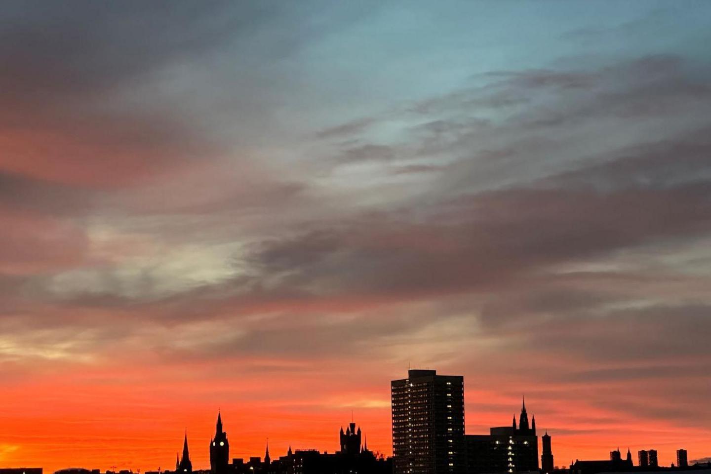 Buildings in Aberdeen, including a tower block, are silhouetted against a sky of orange, grey and blue colours.