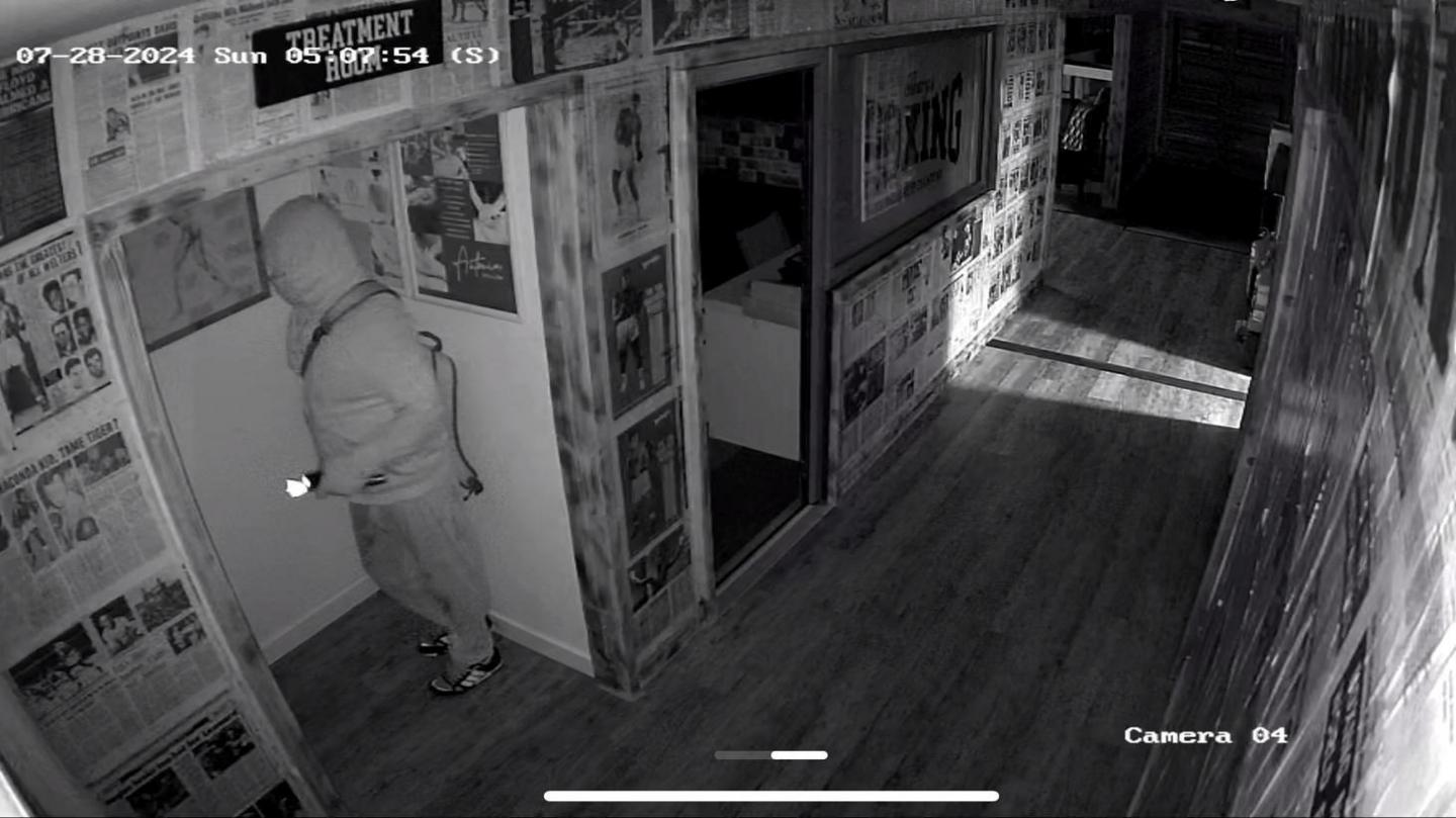 CCTV image of a person standing in the gym building wearing a hoodie