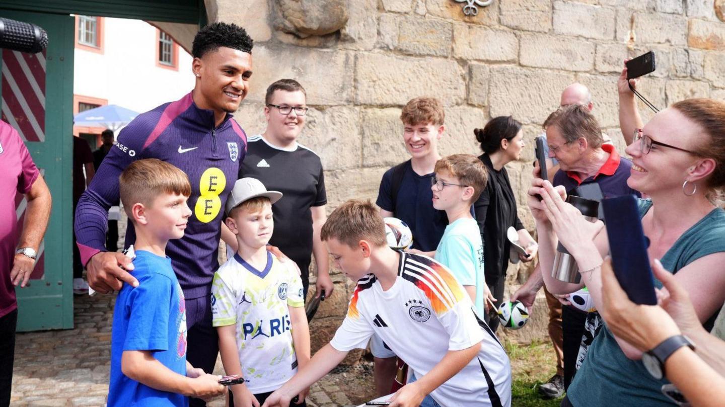 Ollie Watkins greets young children outside while having his photo taken by fans