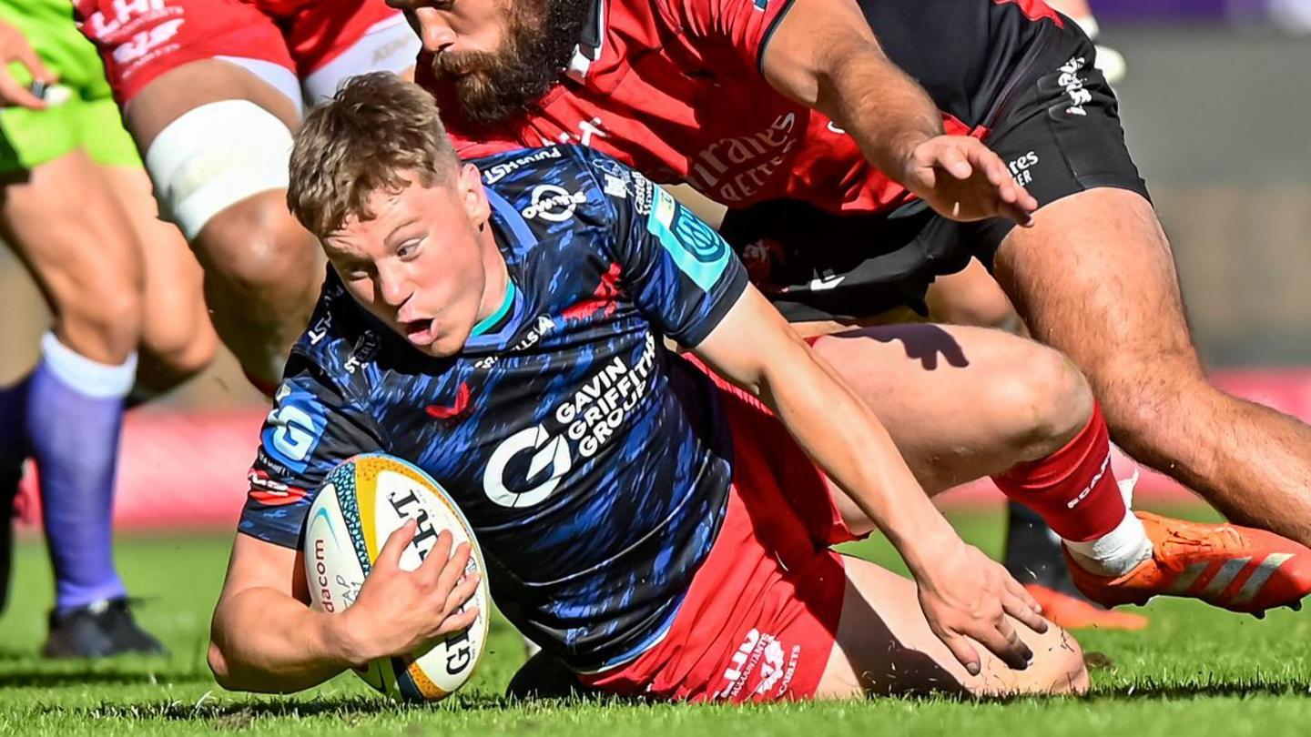 Sam Costelow of the Scarlets is tackled byJaco Visagie of the Emirates Lions