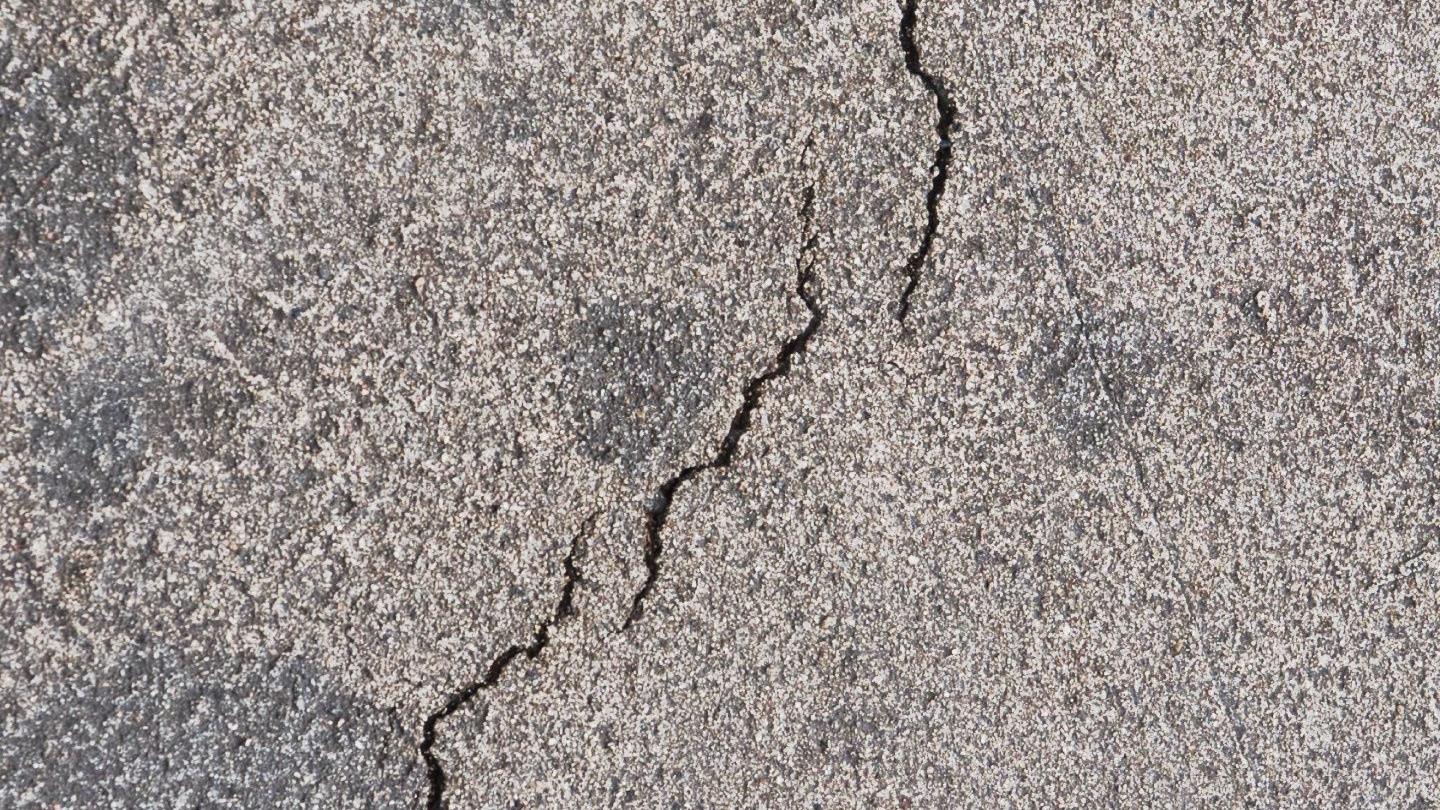 The image shows cracked concrete, with darker grey spots around the line.