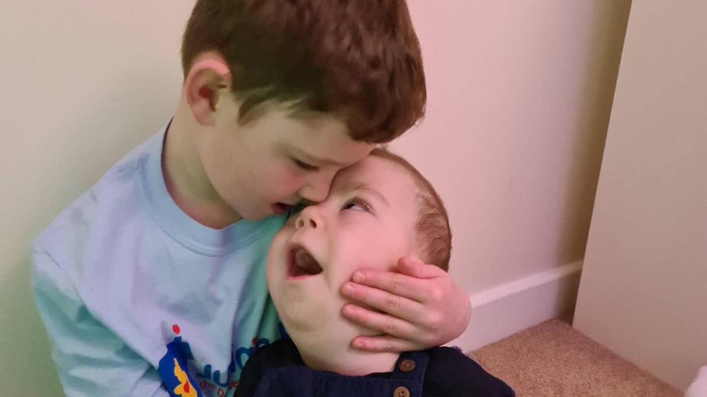 Harry cuddling his brother Reuben. Reuben is looking up at him and Harry is embracing his brother's face.