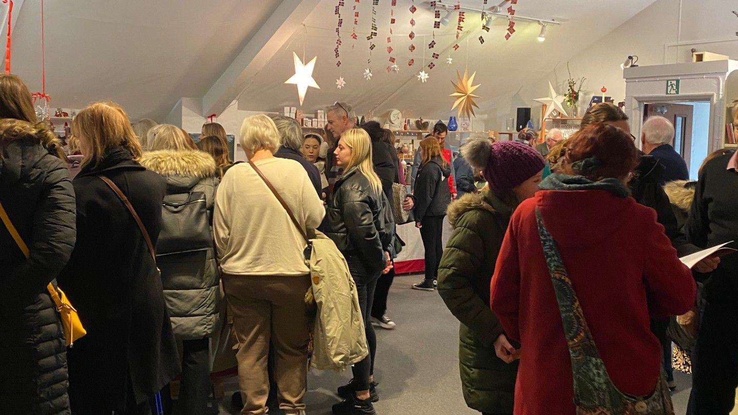 A crowd of people in the Danish Church looking at stalls. There is Christmas bunting hanging from the ceiling. 