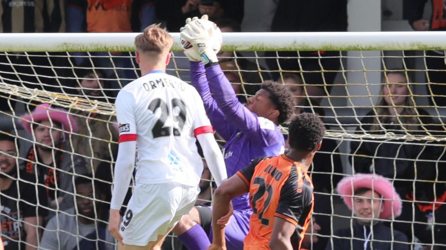 Danny Ormerod in a white AFC Fylde kit challenges a goalkeeper for the ball