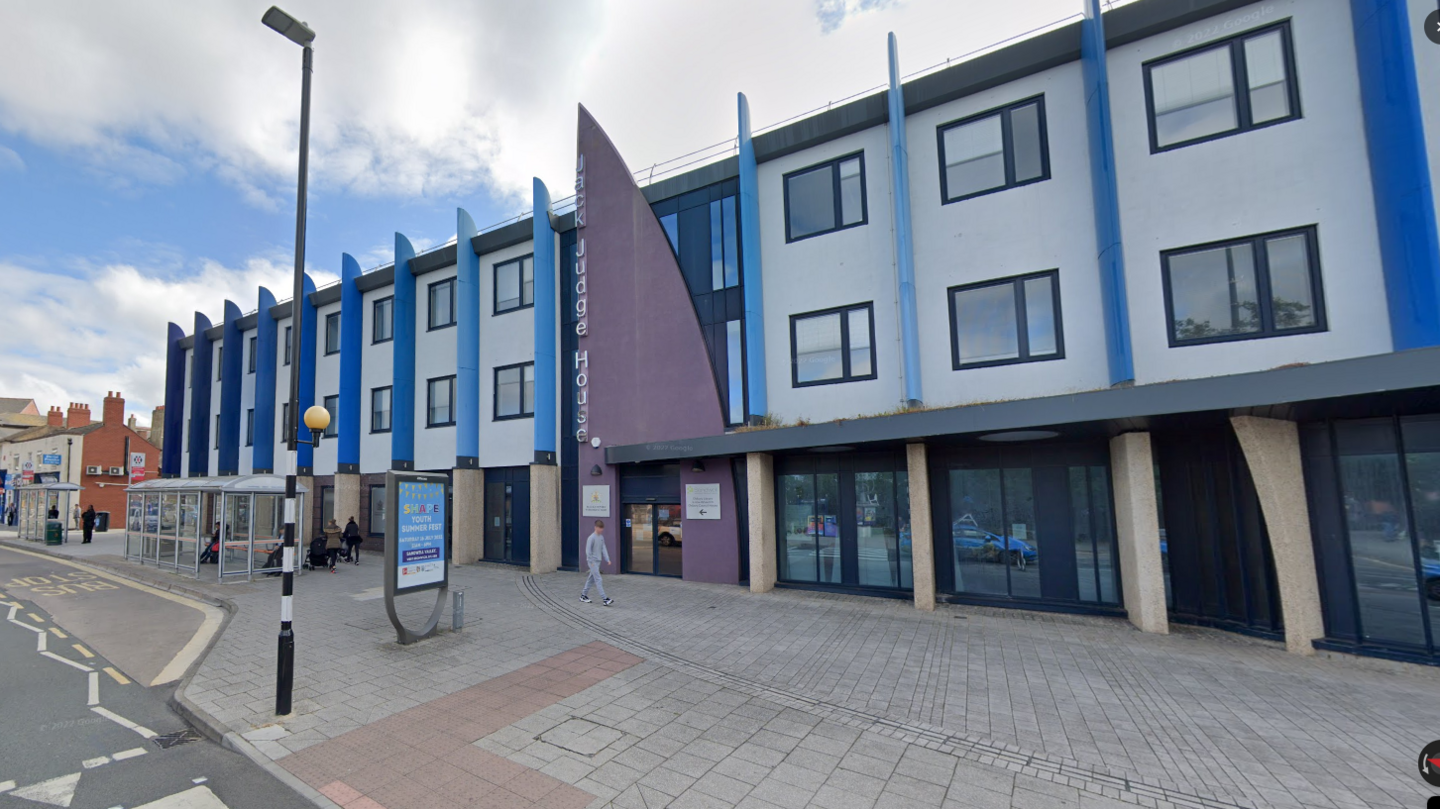 The Black Country Coroner's Court. It is a modern looking building. There is a bus stop nearby and a person walking in the street. 