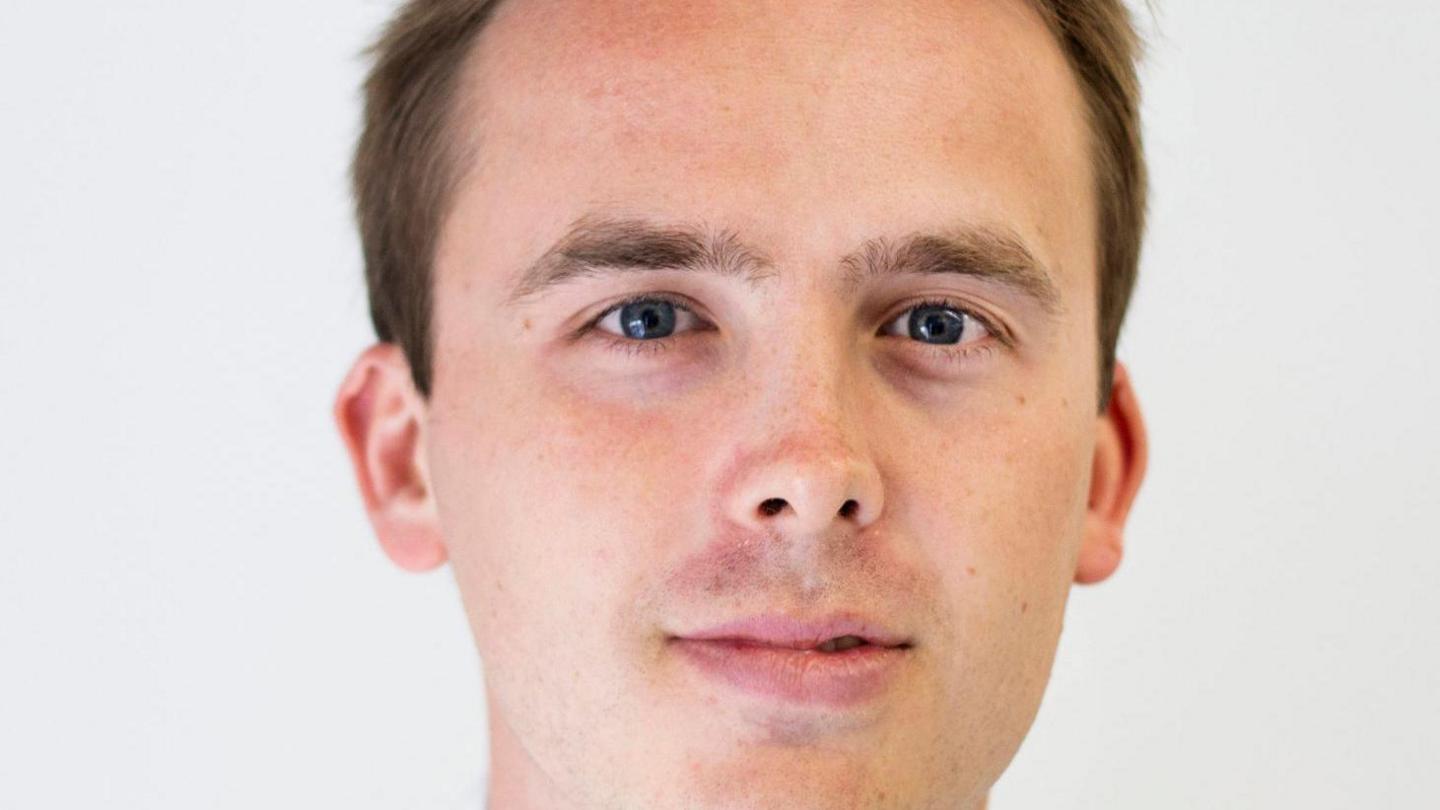 Sam Richardson has brown hair and blue eyes. A close-up shot of his face is shown against a white background as he looks into the camera.
