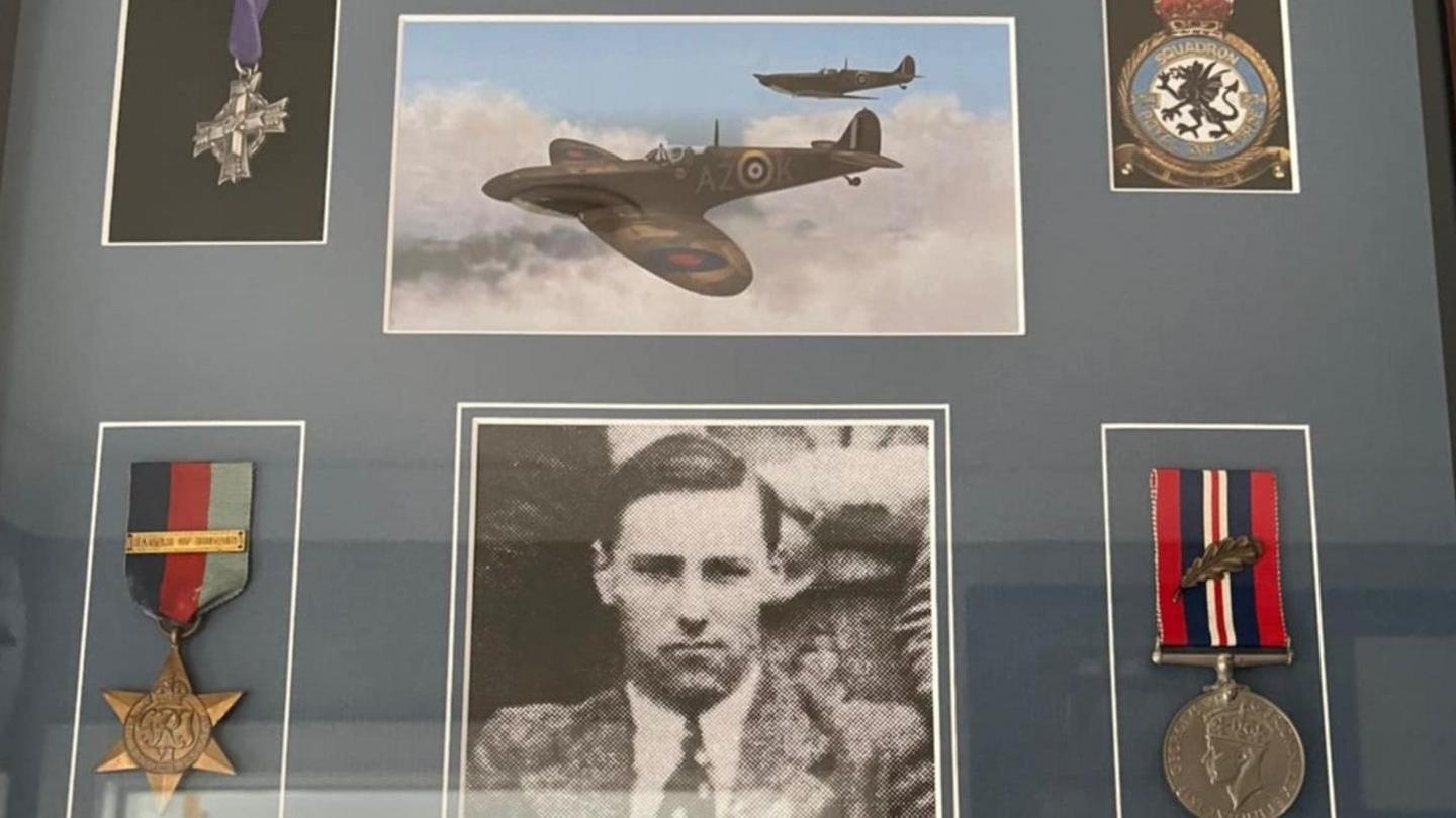 A collection of World War Two medals and photos behind a window cabinet.