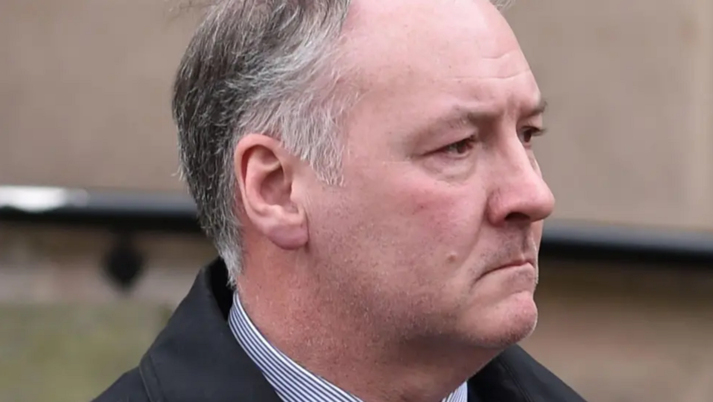 A man with grey hair and a white shirt and dark jacket