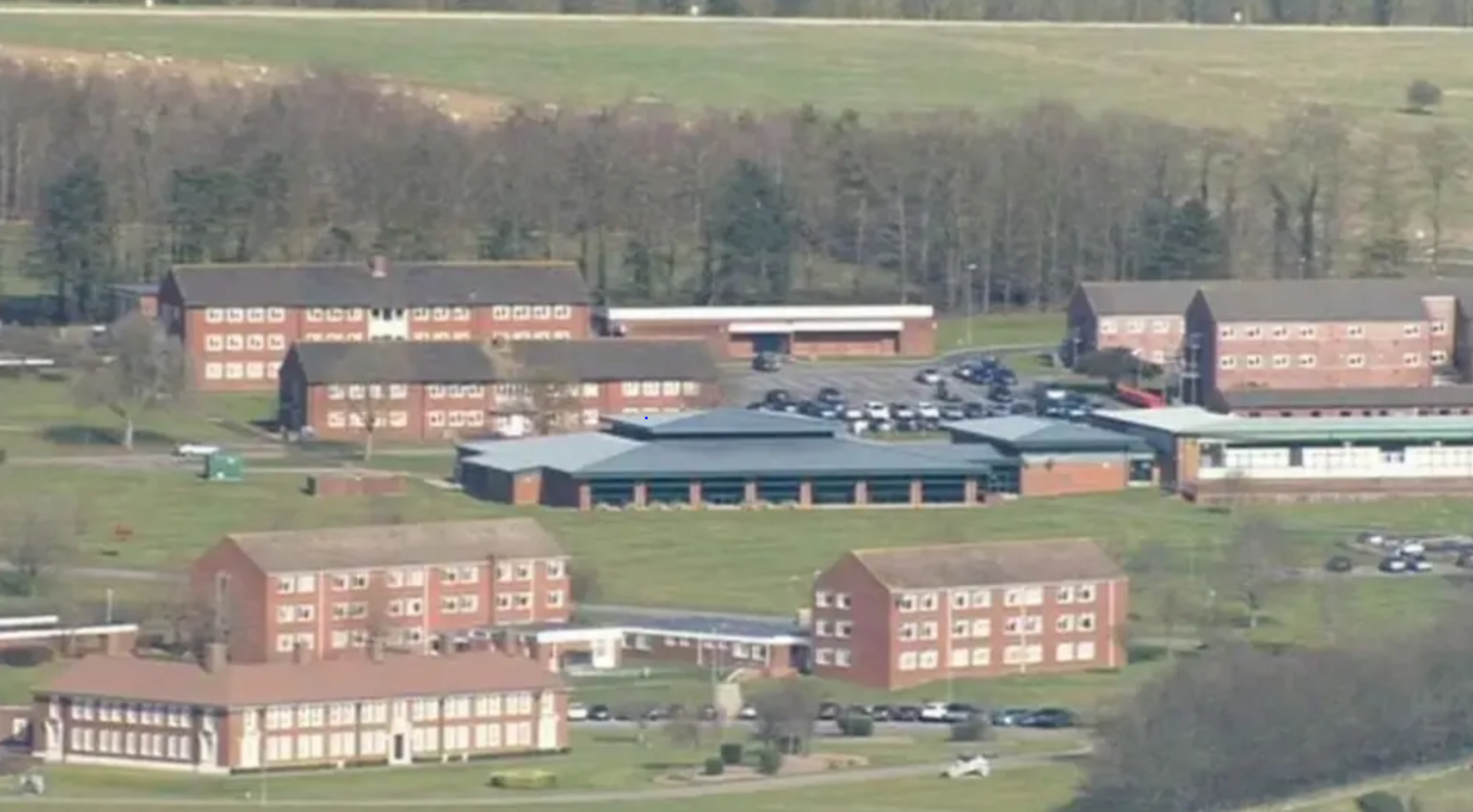 Various brown brick military buildings set amid grass and trees. There are several cars parked near each building and the photo is taken from a long distance away