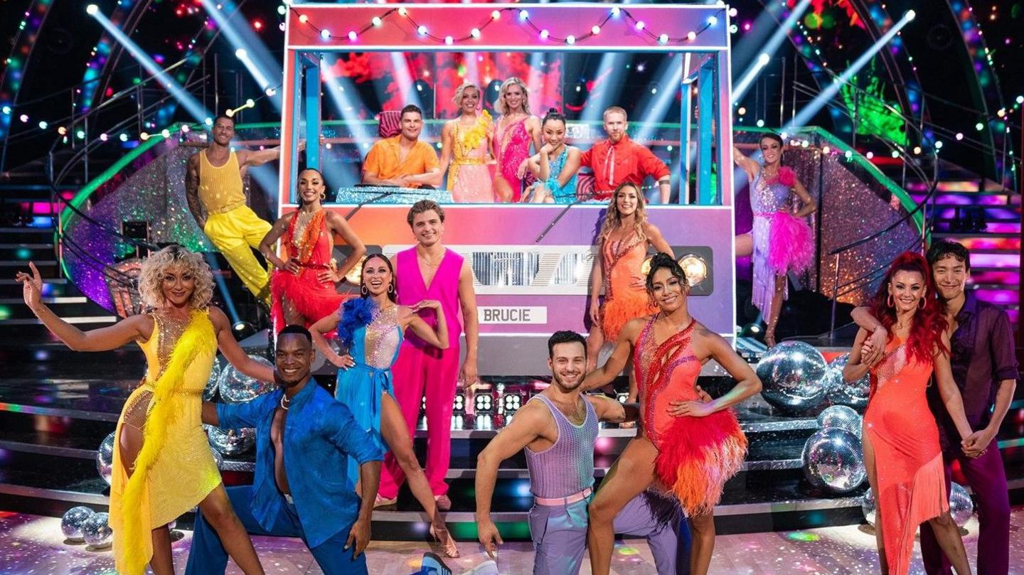 Strictly Come Dancing's professional dancers line up in front of a fake bus front in the studio, wearing colourful costumes