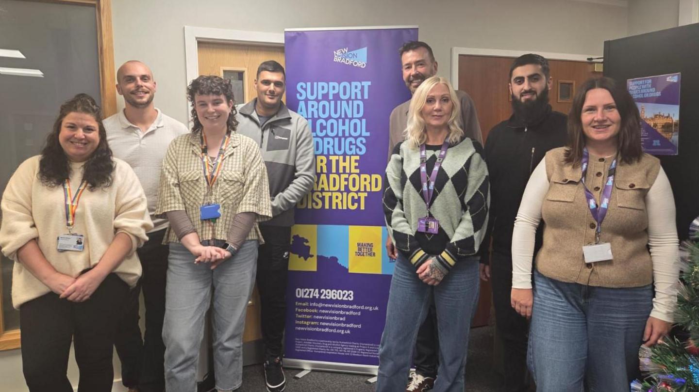 A group of men and women wearing lanyards standing in front of a banner saying "support around alcohol and drugs for the Bradford district".