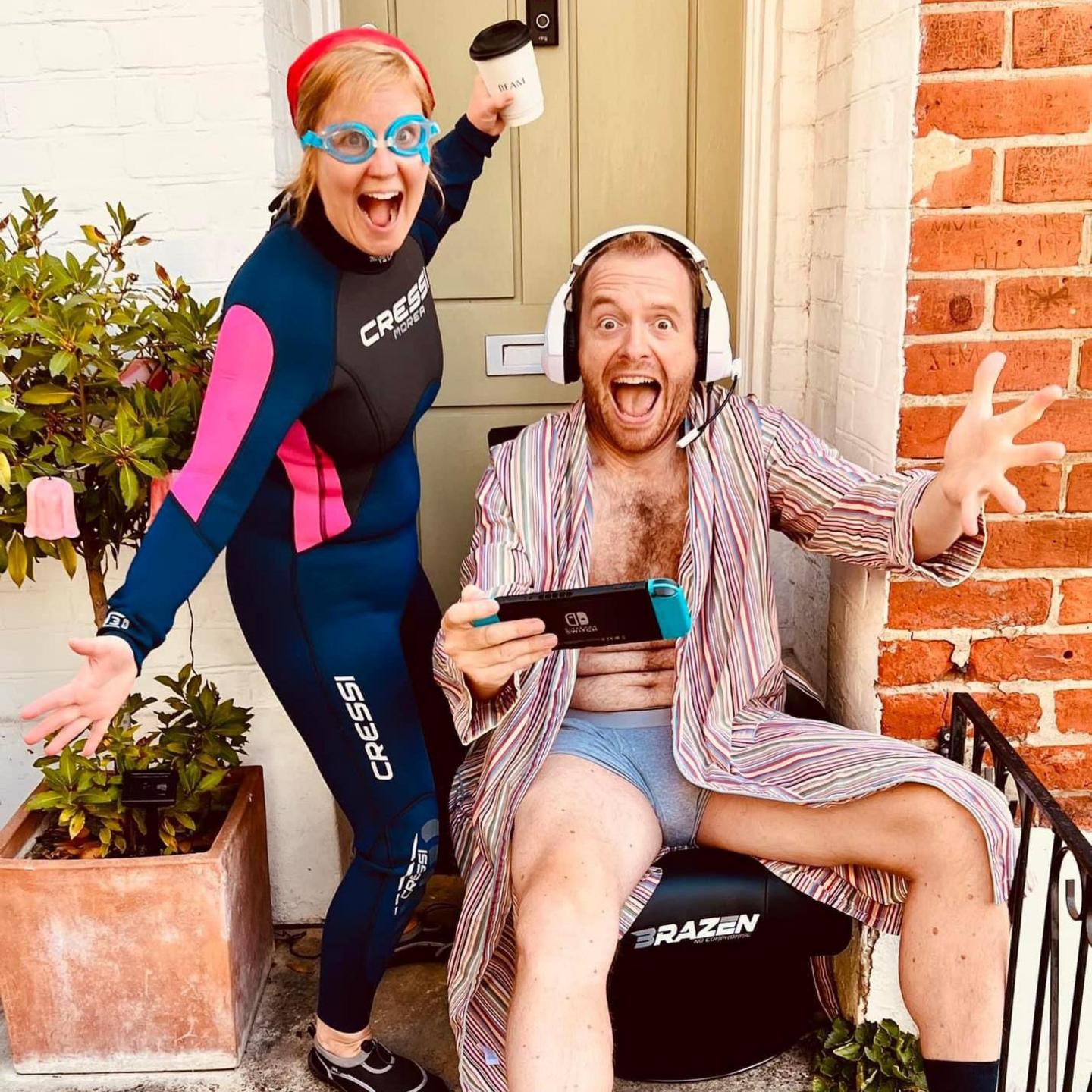 Tom, wearing a striped dressing gown, underwear and a gaming headset, plays on a console, grinning at the camera. Next to him, Beth wears a wetsuit and goggles, holding a coffee cup.
