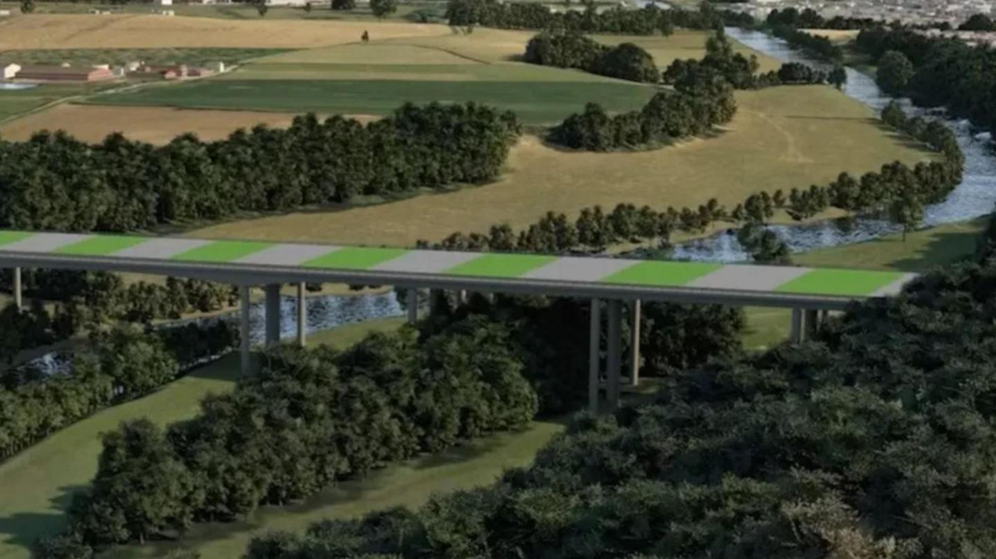 A green and white striped bridge running above trees and fields with a river running underneath