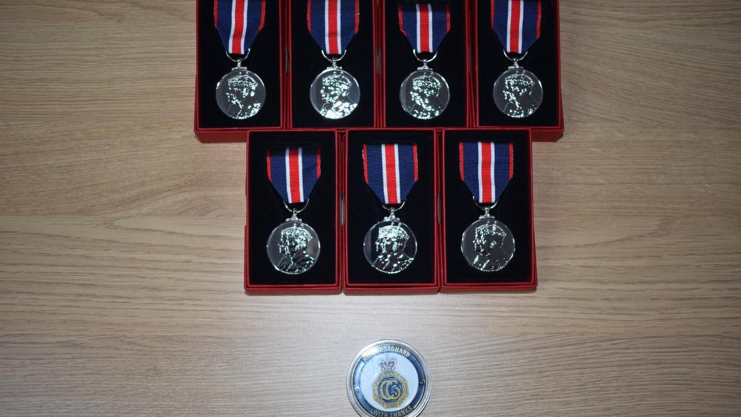 Seven King's Coronation medals of recognition laid in boxes and a commemorative coil on a table