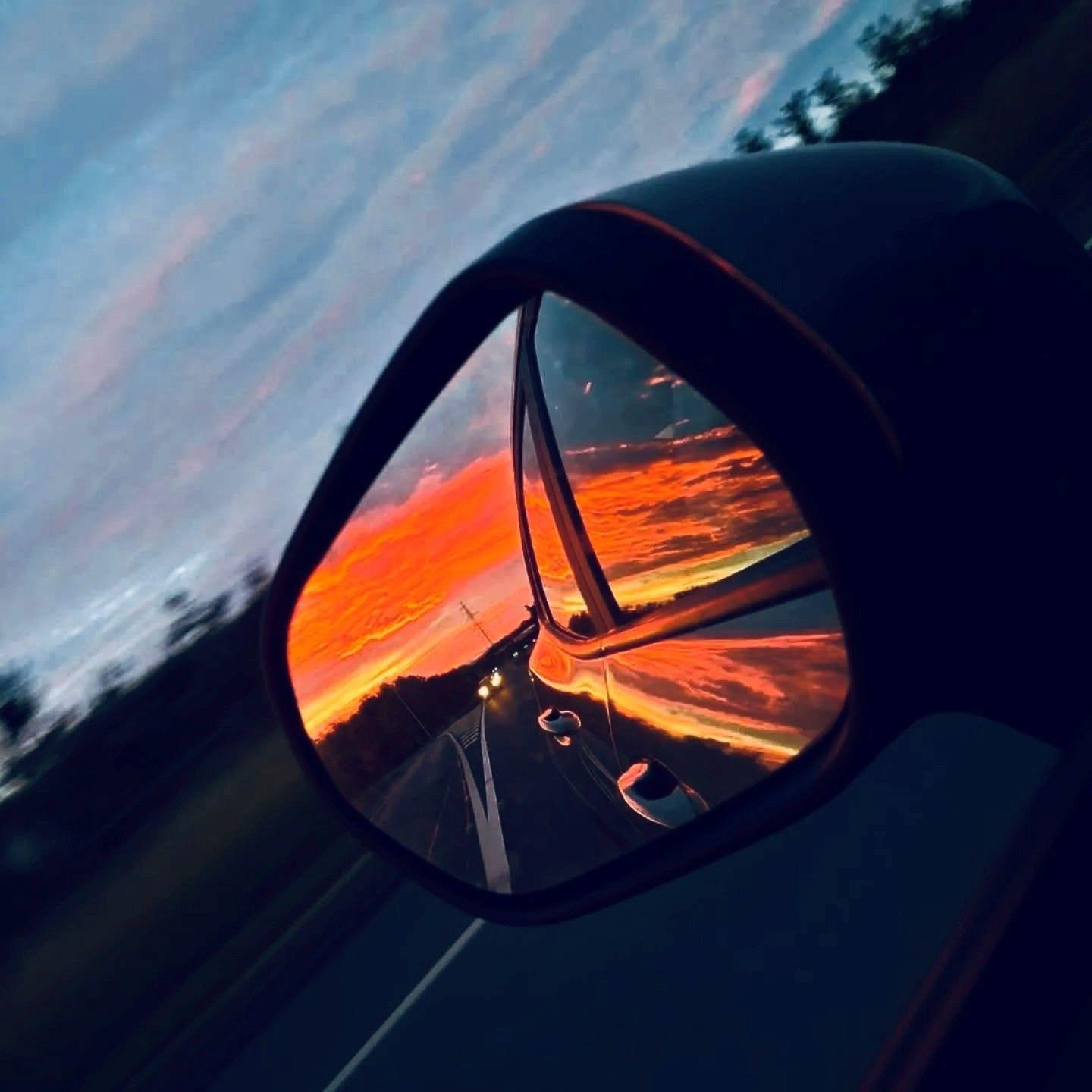 Orange sunset glow in wing mirror of a car as it travels along a road.