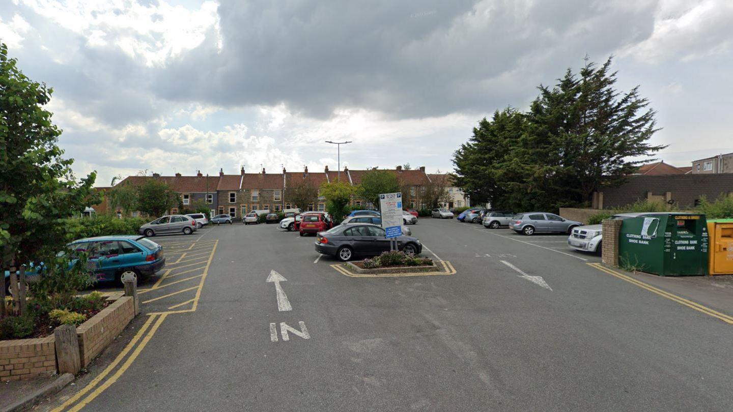 Byron Place car park in Staple Hill. It is a large car park surrounded by residential homes with donation bins visible on the right. The car park is opposite a Tesco.