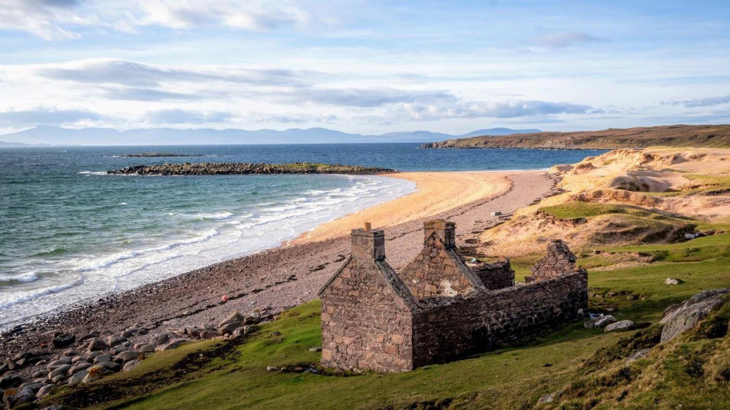 A ruined house on a beach. The sea is crashing in waves on a beach. In the distances are the hills of Skye.