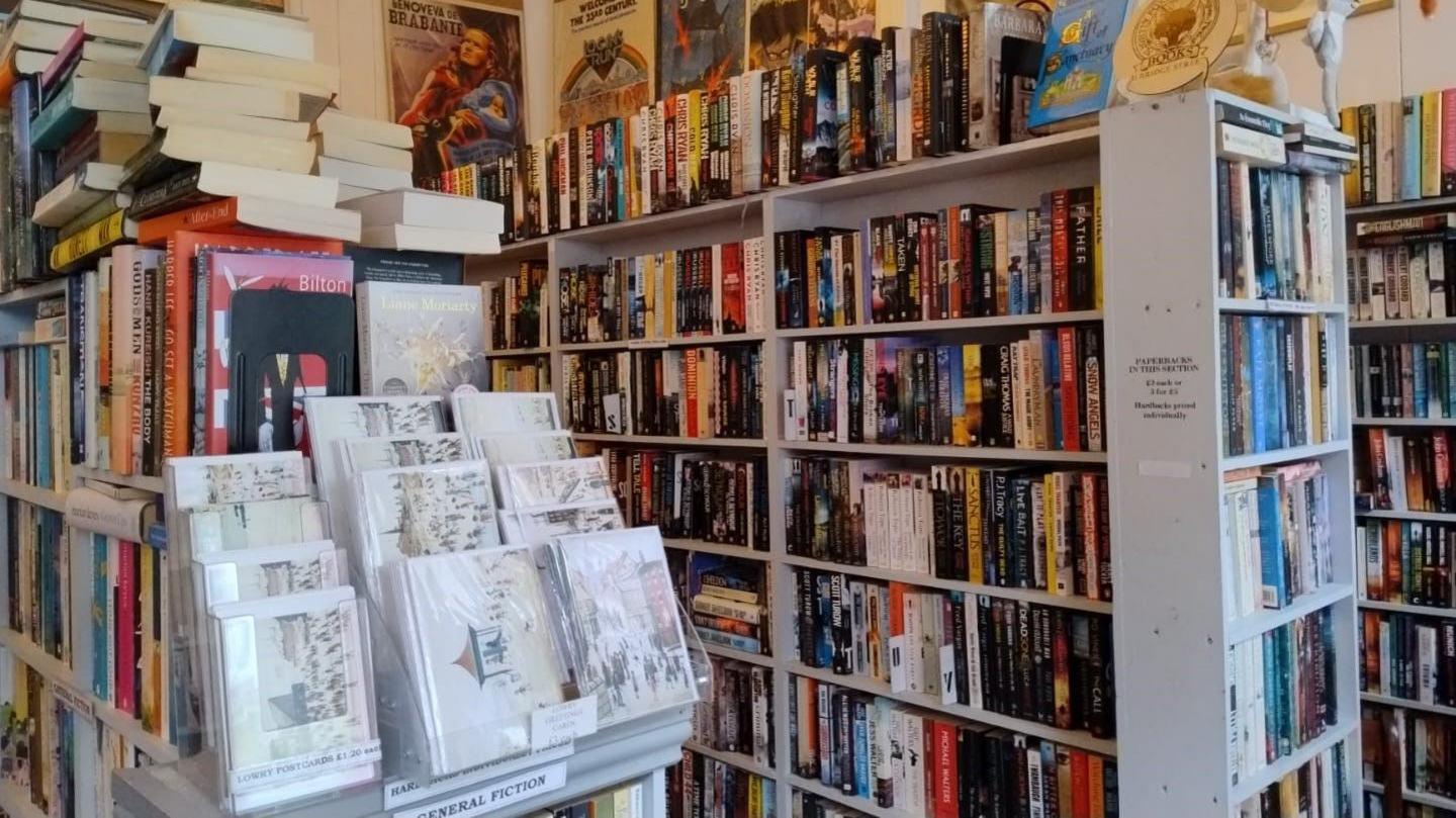 The interior of a bookshop with rows upon rows of books and prints of Lowry in the foreground 