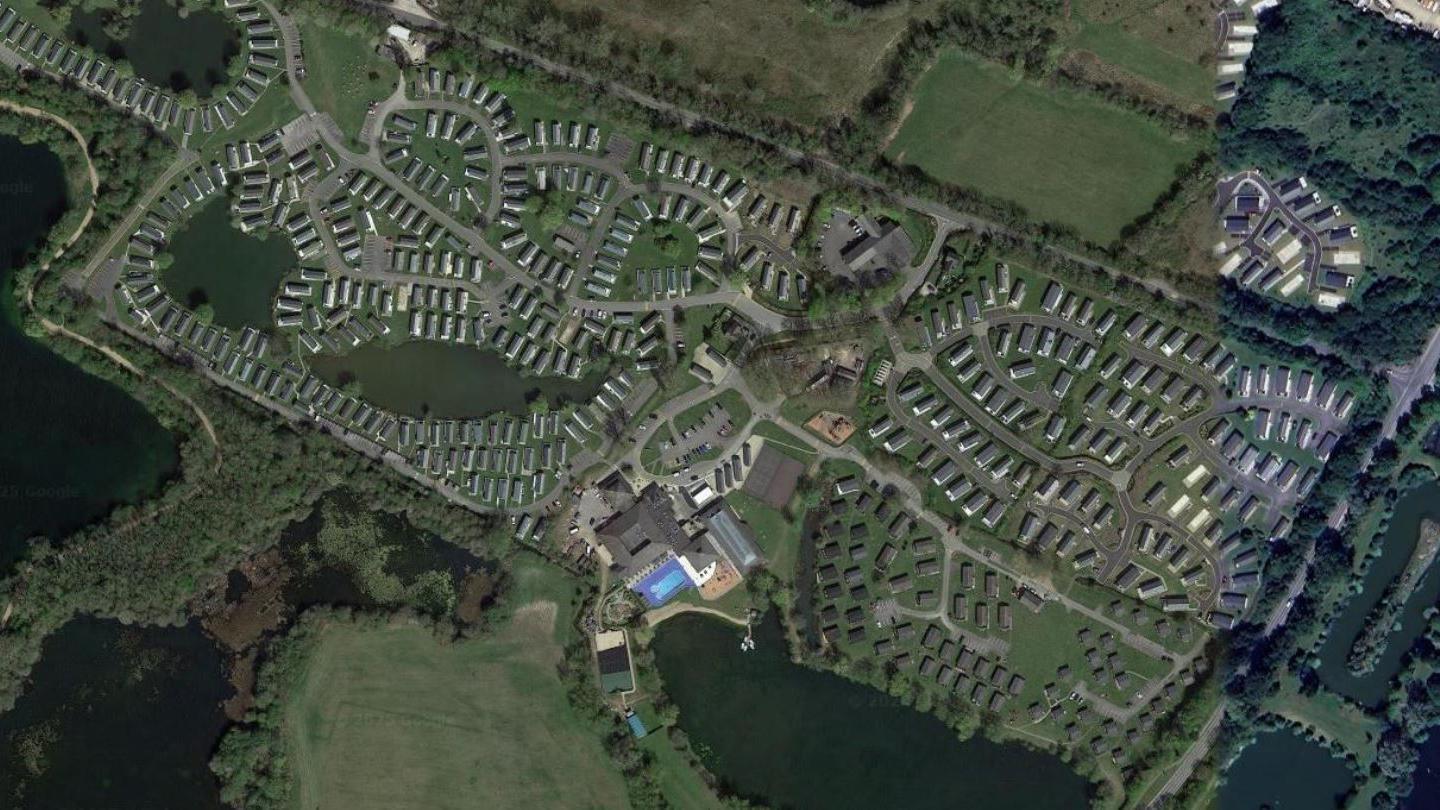 An aerial view taken from Google which shows the massive holiday park. It shows 65 acres of land with several lakes and bodies of water surrounding it. The rectangular site is dotted with hundreds of holiday cabins and there is the reception building and a pool in the centre.