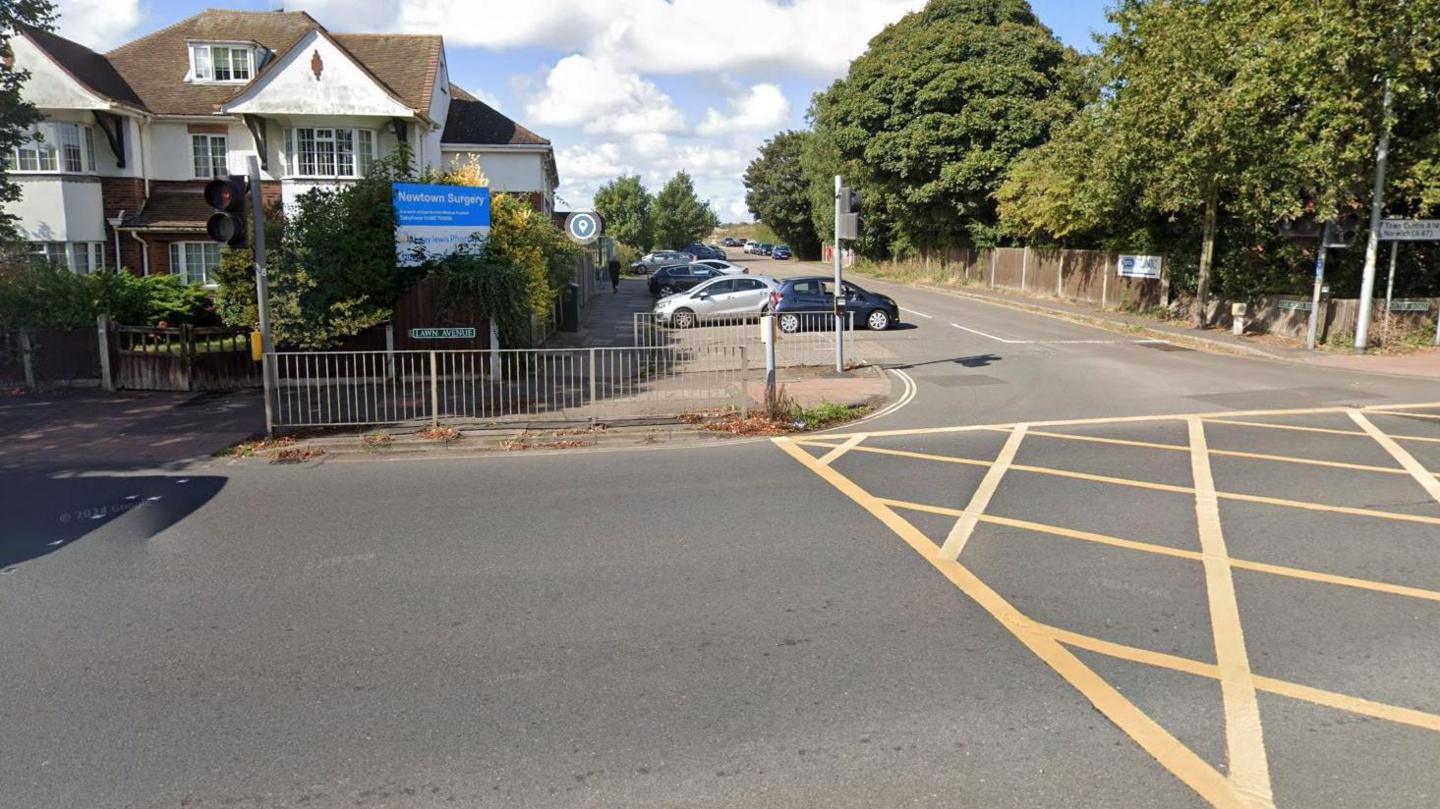 A doctor's surgery, with a blue sign board and railings in front of it, borders the Lawn Avenue road junction