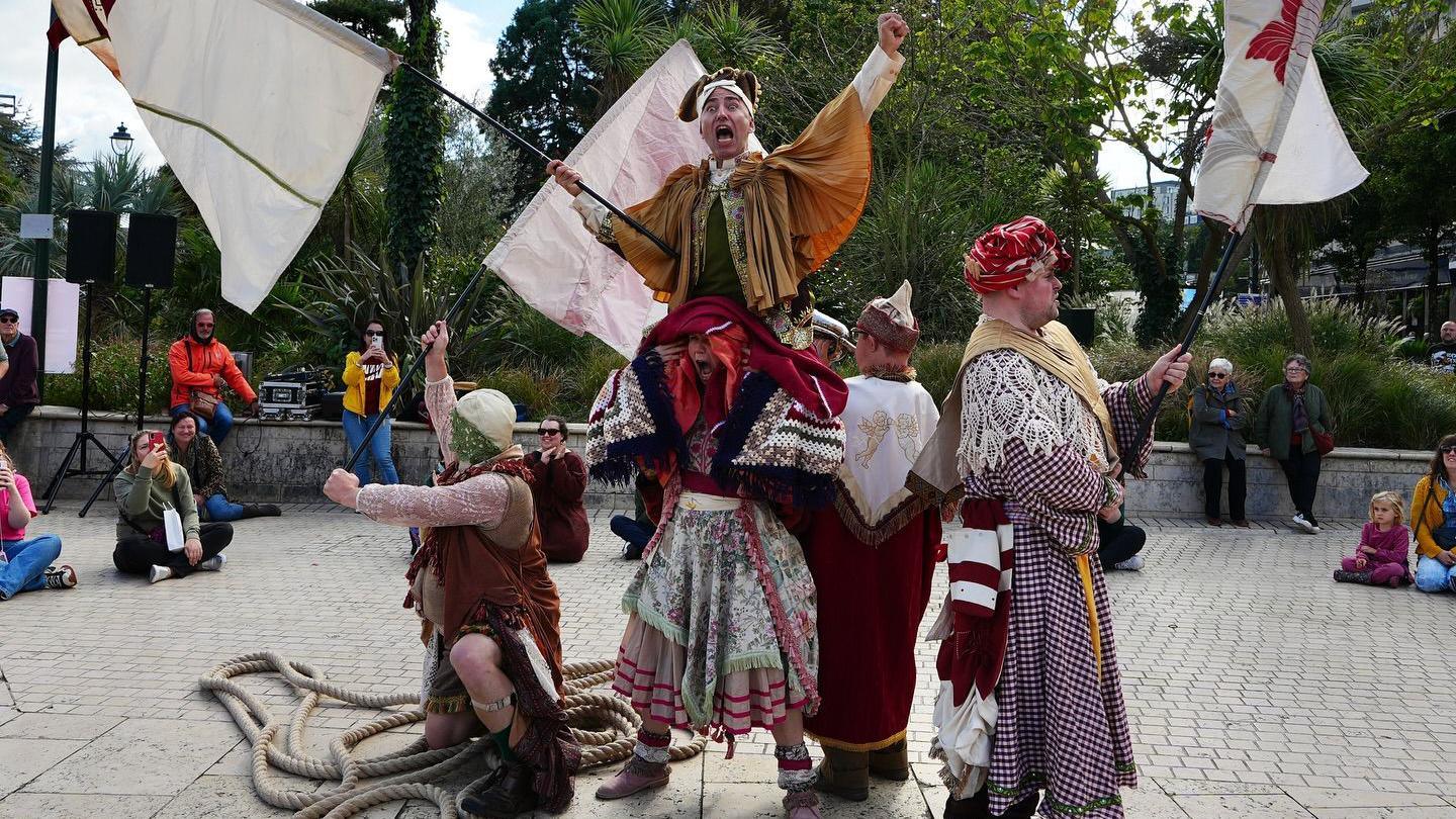 A performance by a group waving flags and chanting while in artistic dress and with people watching them.