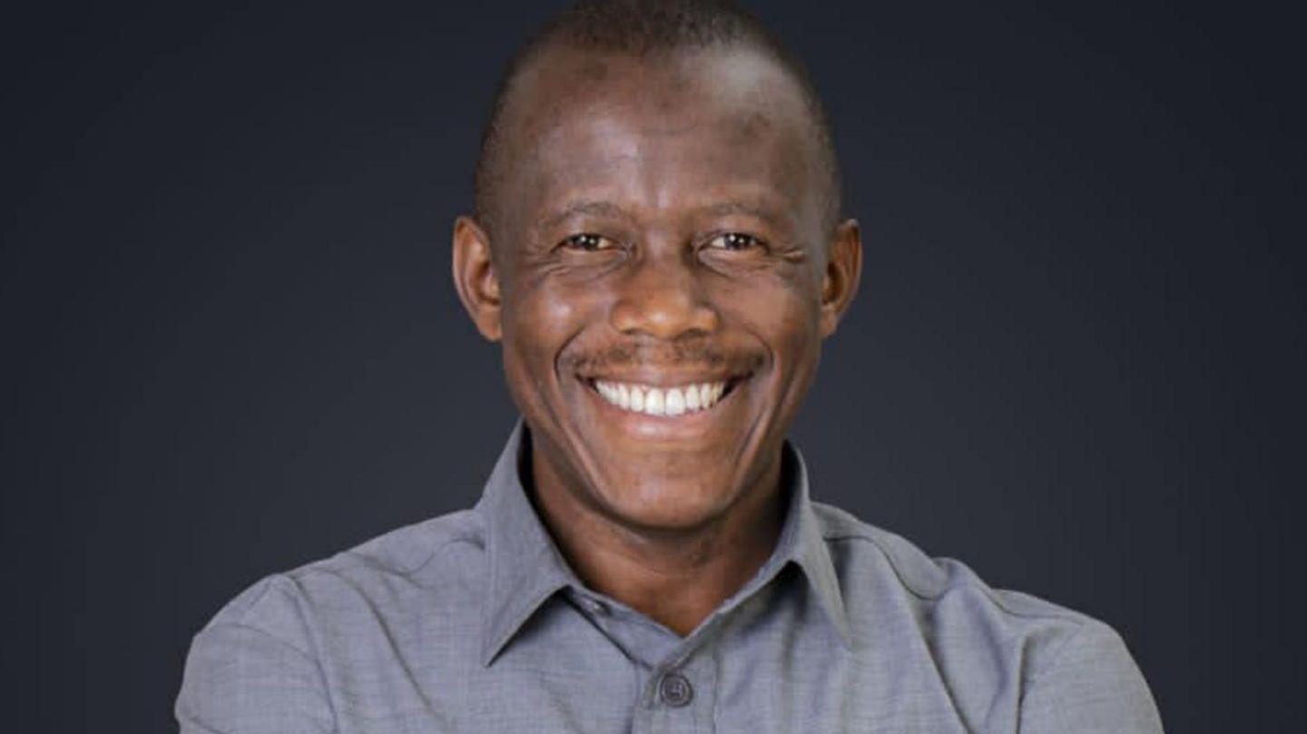 Humphrey Polepole smiles. He is wearing a grey shirt.