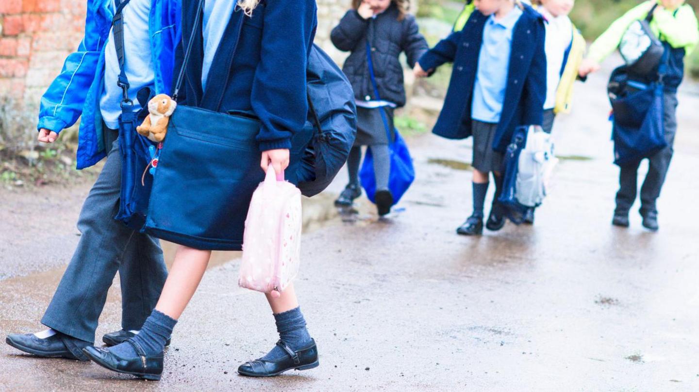 School pupils walking out of school. Some wear trousers and others wear skirts. 