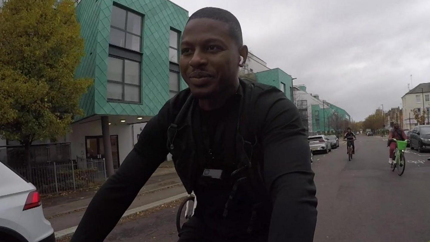 Terrell Lewis cycling along a road, looking straight ahead, followed by two other cyclists. 