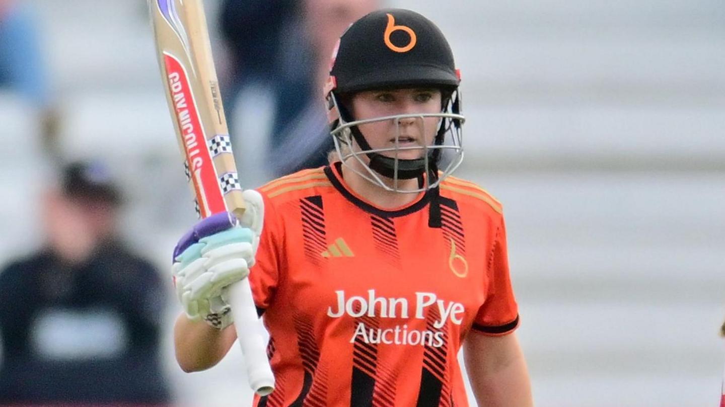 Kathryn Bryce raises her bat after scoring a 50