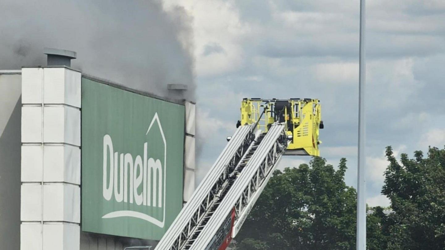 Smoke can be seen billowing from a Dunelm store. An extended cherry picker attached to a fire engine is in the shot.