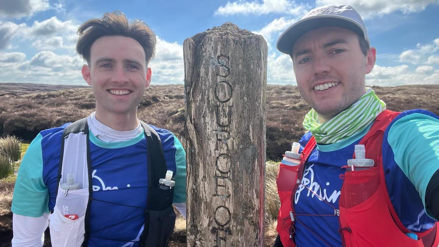 Tom and Cameron stand in front of a sign for the source of the River Severn