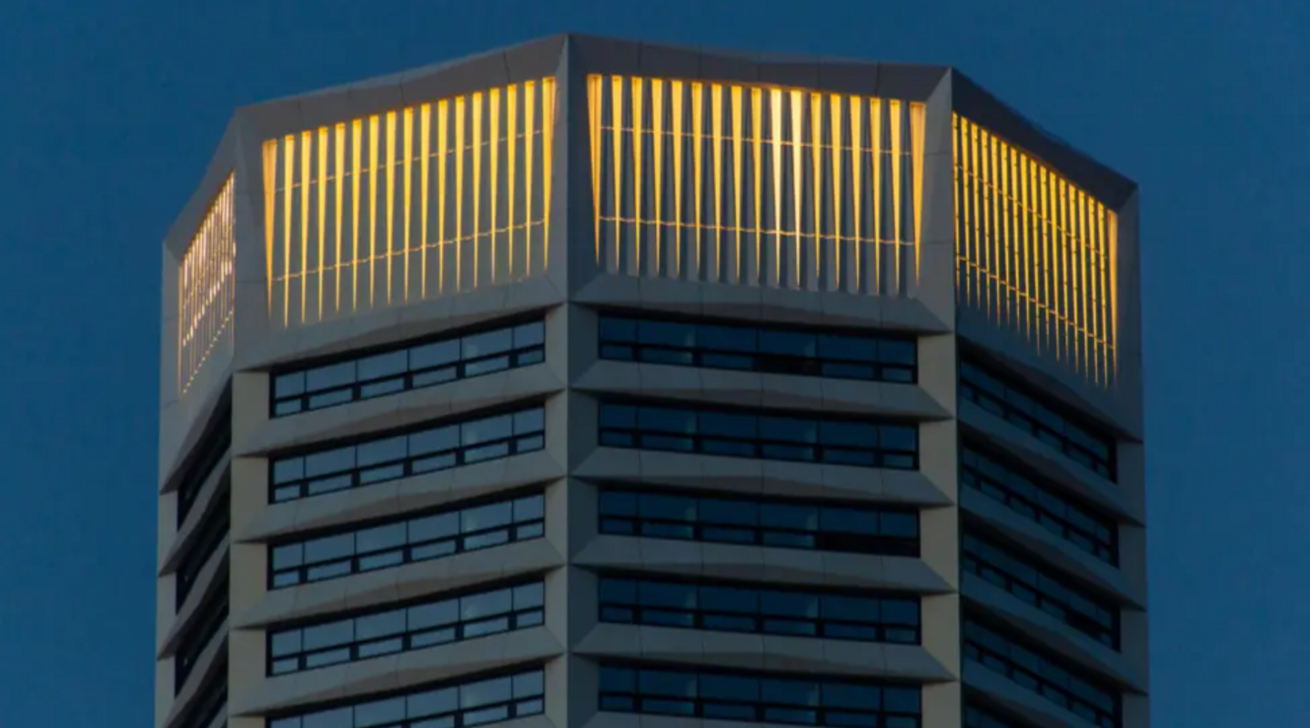 A photo of The Octagon in Birmingham. It is gleaming white with narrow windows. It is an evening and it is set against a dark sky. The crown at the top is bright with lights.