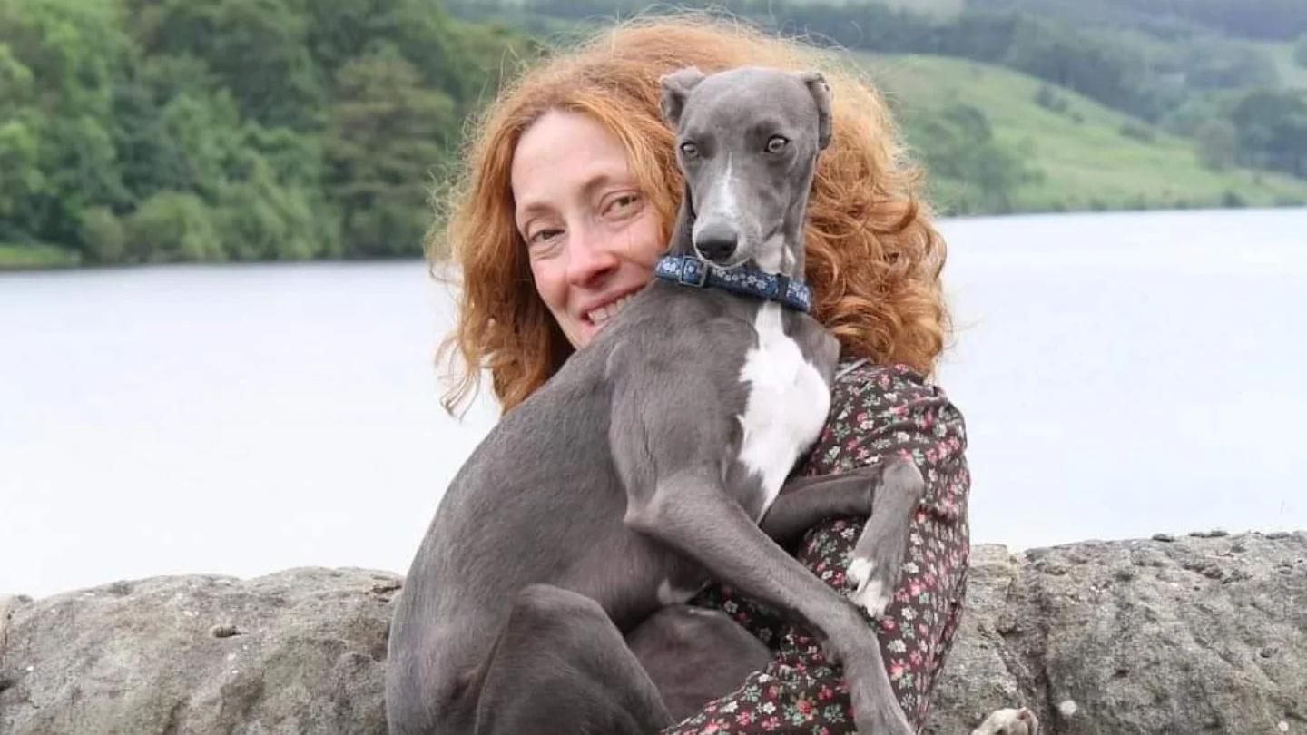 Lucy Gell holding her Italian Greyhound Betsy, Lucy has ginger hair and Betsy is largely dark grey in colour with a white chest. 