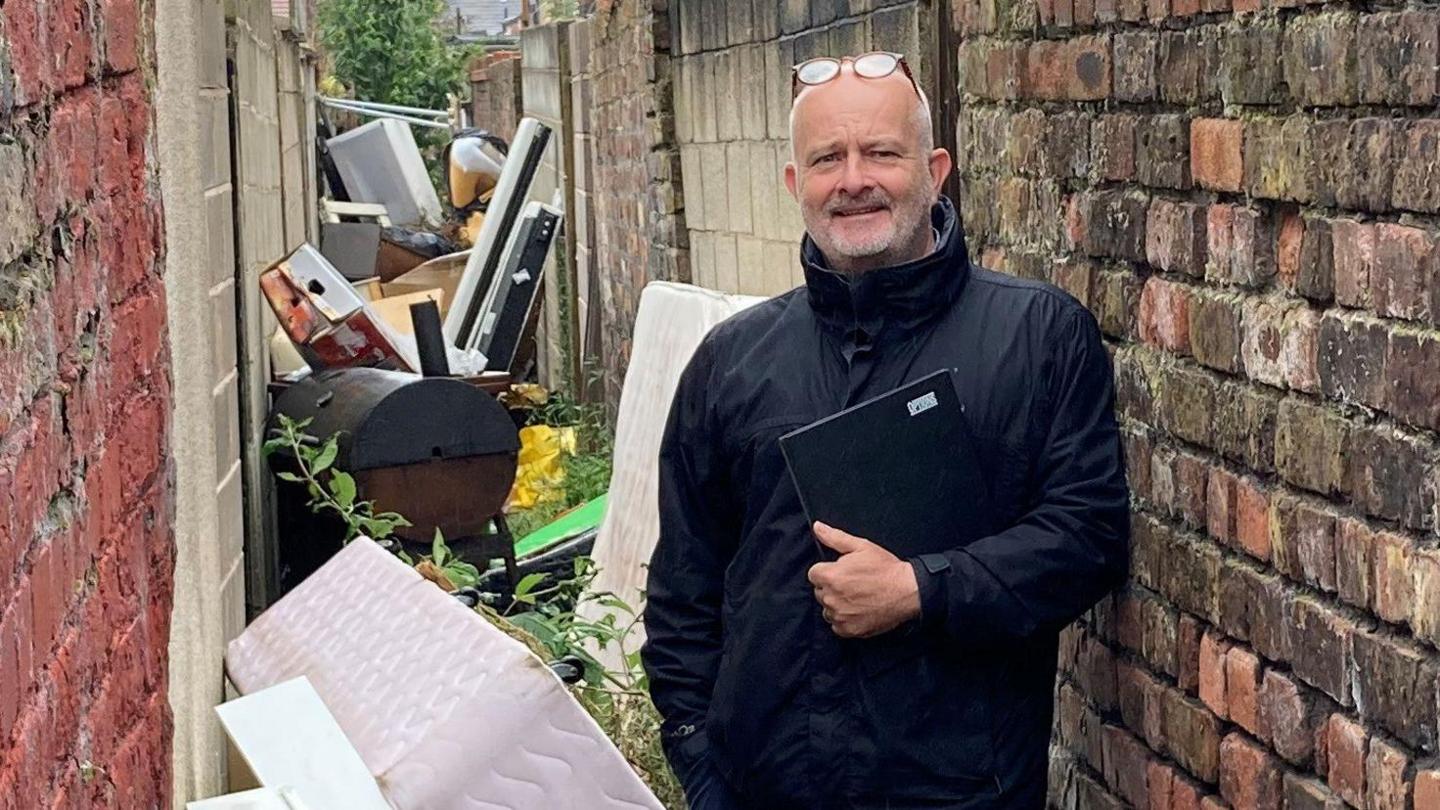 Councillor Peter Harvey stood in an alleyway full of rubbish